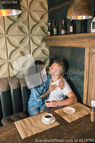 Image of Happy young couple is drinking coffee and smiling while sitting at the cafe