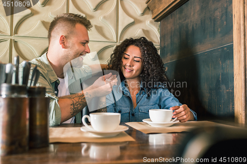 Image of Happy young couple is drinking coffee and smiling while sitting at the cafe