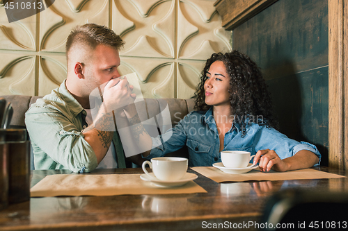 Image of Happy young couple is drinking coffee and smiling while sitting at the cafe