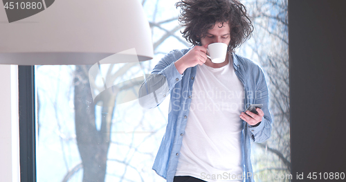 Image of young man drinking coffee and using a mobile phone  at home