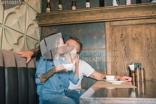 Image of Happy young couple is drinking coffee and smiling while sitting at the cafe