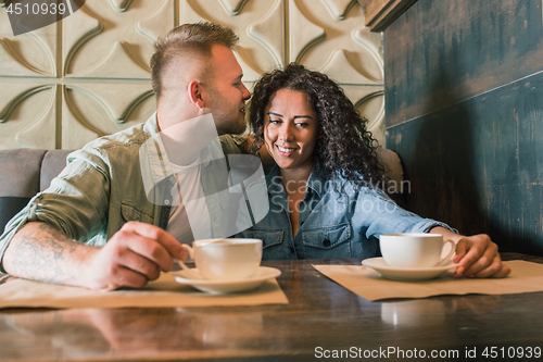 Image of Happy young couple is drinking coffee and smiling while sitting at the cafe