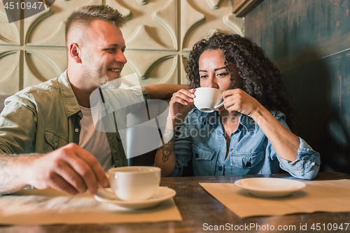 Image of Happy young couple is drinking coffee and smiling while sitting at the cafe