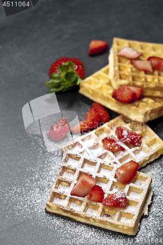 Image of Belgium waffers with strawberries and sugar powder on black boar