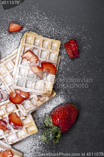 Image of Belgium waffers with strawberries and sugar powder on black boar