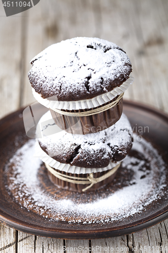 Image of Chocolate dark muffins with sugar powder on brown plate on rusti