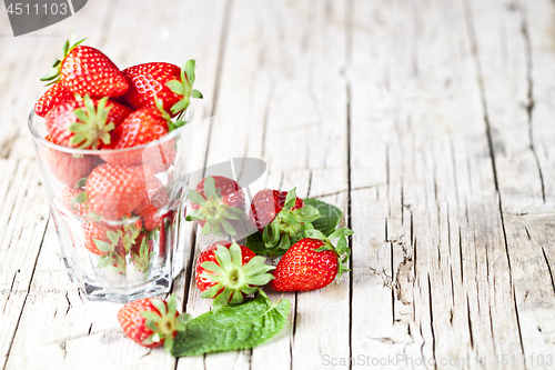 Image of Organic red strawberries in glass and mint leaves on rustic wood