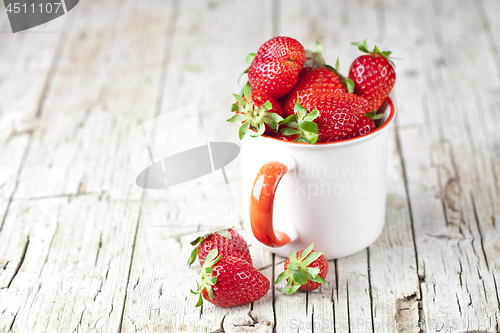 Image of Organic red strawberries in white ceramic cup on rustic wooden b