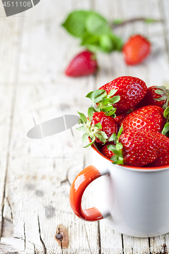 Image of Organic red strawberries in white ceramic cup on rustic wooden b