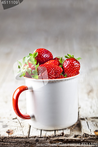 Image of Organic red strawberries in white ceramic cup on rustic wooden b