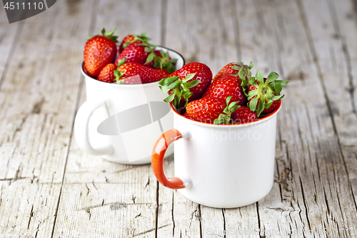 Image of Organic red strawberries in two white ceramic cups on rustic woo