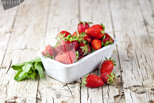 Image of Fresh red strawberries in white bowl and mint leaves on rustic w