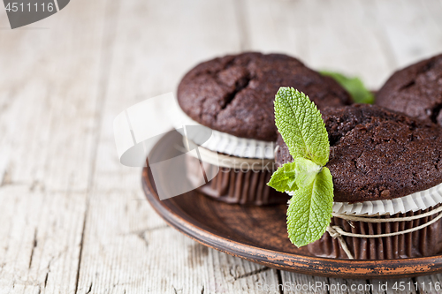 Image of Chocolate dark muffins with mint leaves on brown ceramic plate.