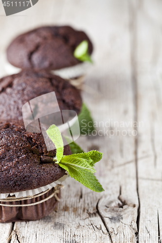 Image of Chocolate dark muffins with mint leaves closeup on rustic wooden