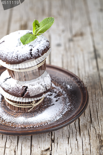 Image of Chocolate dark muffins with sugar powder and mint leaf on brown 