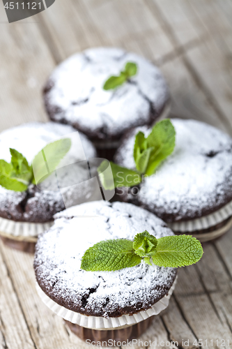 Image of Chocolate dark muffins with sugar powder and mint leaf on rustic