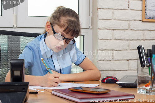 Image of An eight-year-old girl at the table in the office writes a fountain pen on a piece of paper