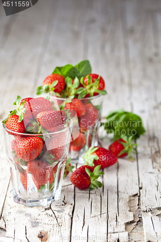 Image of Organic red strawberries in two glasses and mint leaves on rusti