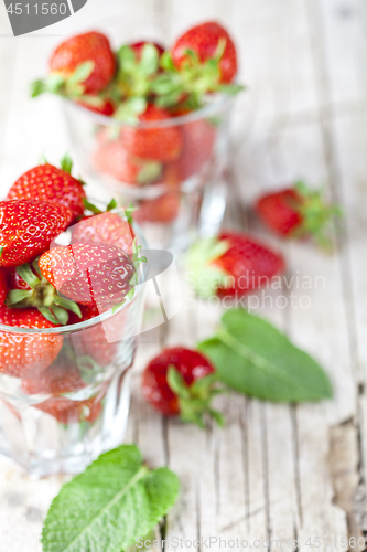 Image of Organic red strawberries in two glasses and mint leaves on rusti