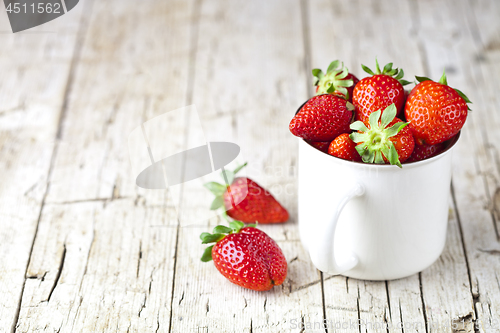 Image of Organic red strawberries in white ceramic cup on rustic wooden b