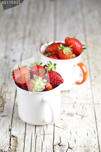 Image of Organic red strawberries in two white ceramic cups on rustic woo