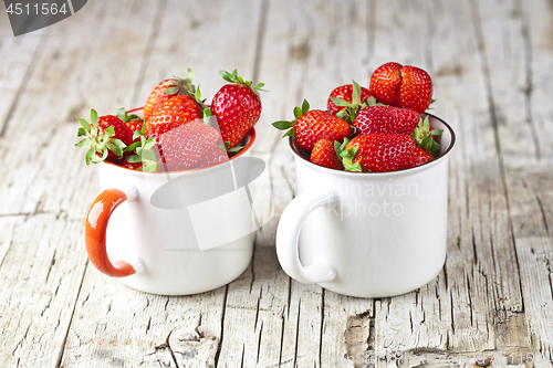 Image of Organic red strawberries in white ceramic cups on rustic wooden 