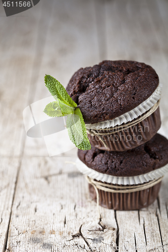 Image of Chocolate dark muffins with mint leaves on rustic wooden table.