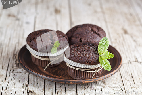 Image of Three chocolate dark muffins with mint leaves on brown ceramic p