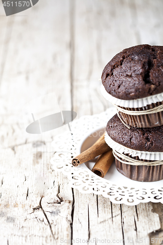 Image of Fresh dark chocolate muffins with cinnamon sticks on white plate