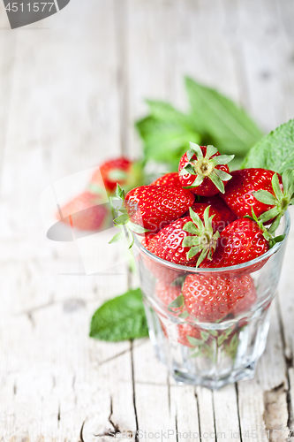 Image of Organic red strawberries in glass and mint leaves on rustic wood