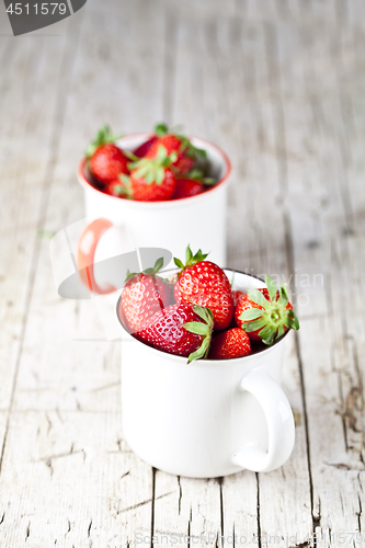 Image of Organic red strawberries in two white ceramic cups on rustic woo