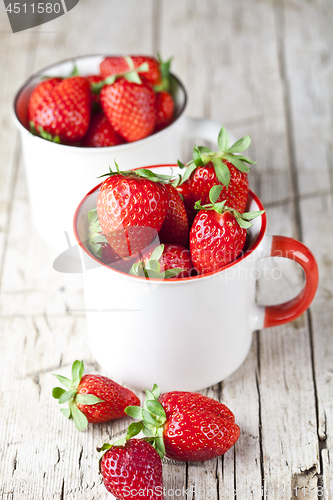 Image of Organic red strawberries in two white ceramic cups on rustic woo