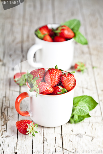 Image of Organic red strawberries in two white ceramic cups and mint leav