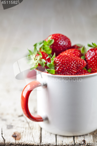 Image of Organic red strawberries in white ceramic cup on rustic wooden b