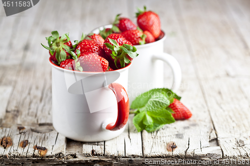 Image of Organic red strawberries in two white ceramic cups and mint leav