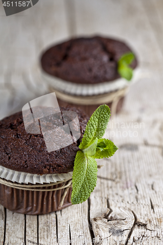 Image of Chocolate dark muffins with mint leaves closeup on rustic wooden