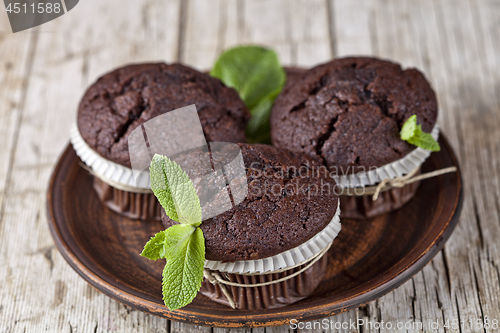 Image of Three chocolate dark muffins with mint leaves on brown ceramic p