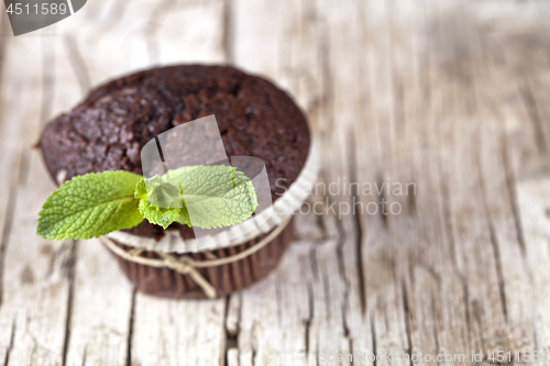 Image of Chocolate dark muffins with mint leaves on rustic wooden table.