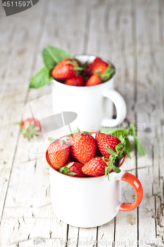 Image of Organic red strawberries in two white ceramic cups and mint leav