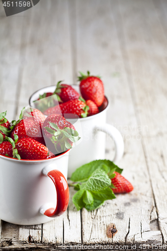 Image of Organic red strawberries in two white ceramic cups and mint leav