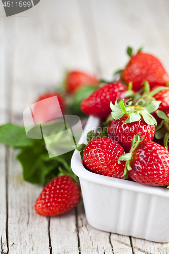 Image of Fresh red strawberries in white bowl and mint leaves on rustic w