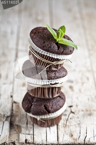 Image of Three fresh dark chocolate muffins with mint leaves on rustic wo
