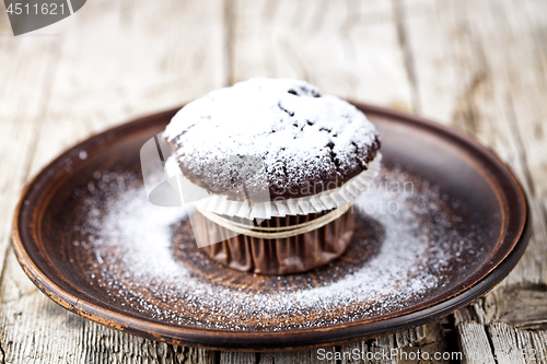 Image of Dark chocolate muffin with sugar powder on brown plate.