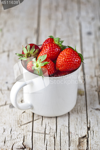 Image of Organic red strawberries in white ceramic cup on rustic wooden b