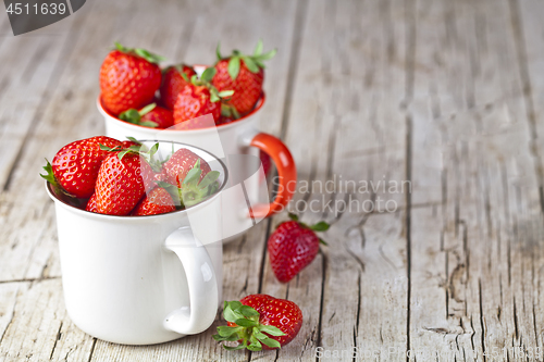 Image of Organic red strawberries in two white ceramic cups on rustic woo