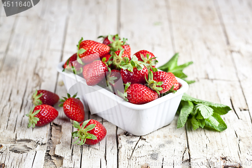 Image of Fresh red strawberries in white bowl and mint leaves on rustic w