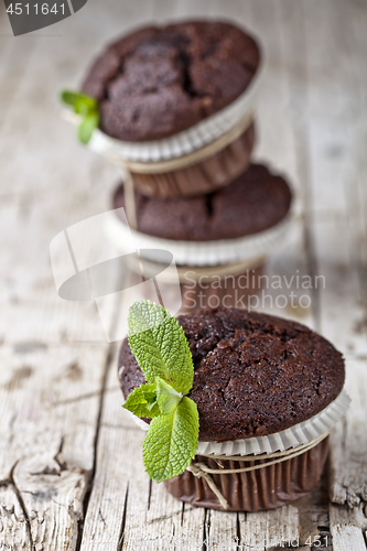 Image of Three fresh dark chocolate muffins with mint leaves on rustic wo