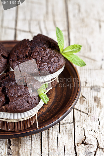 Image of Chocolate dark muffins with mint leaves on brown ceramic plate c