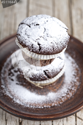 Image of Dark chocolate muffins with sugar powder on brown plate on rusti