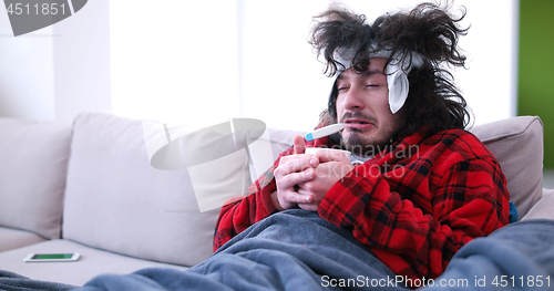 Image of sick man is holding a cup while sitting on couch